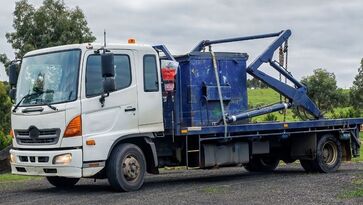 Picture of a skip bin truck - We provide a wide range of skip bins to suit all types of household and business waste disposal requirements. Our skips are available in a variety of sizes, with different compartments that can be used for separate types of waste or mixed loads. 